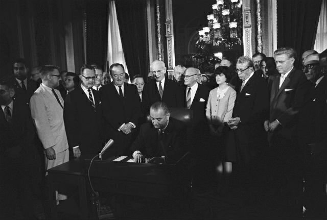 President Lyndon B. Johnson seated at bill signing table as others look on from behind him. (credit: LBJ Library)